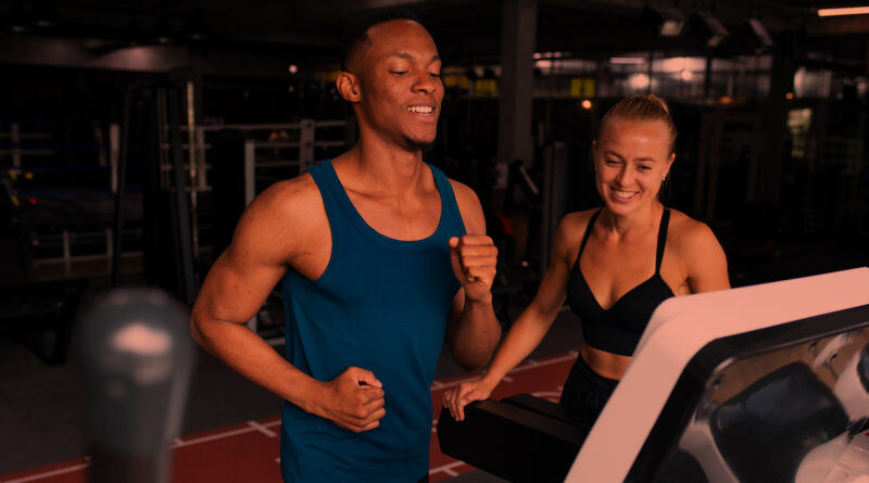 Homem negro correndo na esteira ao lado de personal trainer