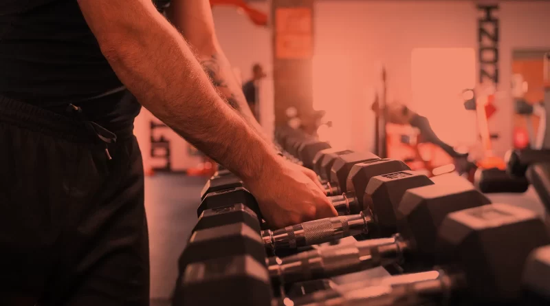 Homem pegando halteres em treino avulso. Foto: Freepik