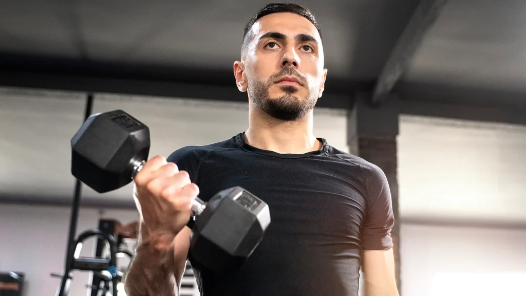 Homem treinando braço com halteres em treino avulso. Foto: Magnific